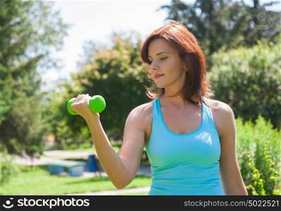 Woman doing exercise with dumbbell outdoors