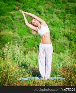 Woman doing exercise yoga outdoors in fresh green park on mountain background, with closed eyes slope in side, body and soul care