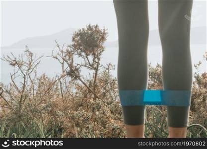 Woman doing exercises in the forest with a rubber band during a spring sunny day with copy space