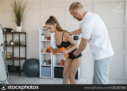 woman doing exercises with male physiotherapist holding dumbbells