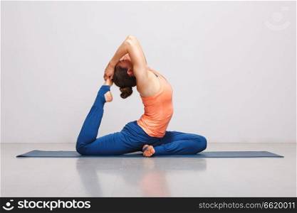 Woman doing Hatha yoga asana Eka pada rajakapotasana - one-legged king pigeon pose on yoga mat on yoga mat in studio on grey bagckground. Woman doing Hatha yoga asana Eka pada rajakapotasana 