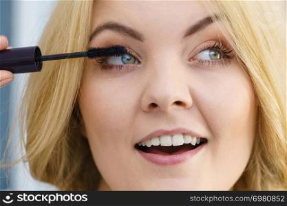 Woman doing her make up using black mascara brushing eyelashes. Female beauty visage concept.. Woman using mascara on her eyelashes