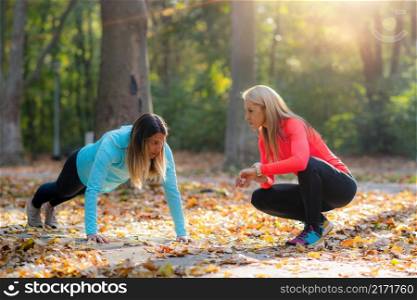 Woman Doing Push-ups, Personal Fitness Trainer Looking at a Smart Watch During Training in the Park. . Trainer Looking at a Smart Watch During Training in the Park.