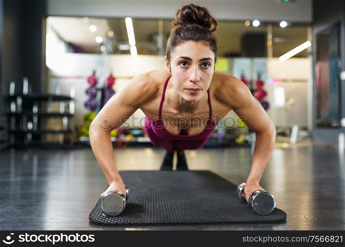 Woman doing push-ups with dumbbells in a fitness workout. Woman doing push-ups exercise with dumbbell in a fitness workout