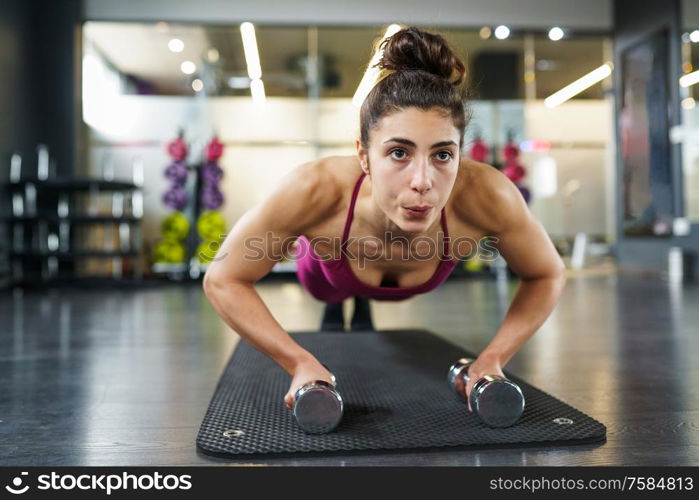 Woman doing push-ups with dumbbells in a fitness workout. Woman doing push-ups exercise with dumbbell in a fitness workout