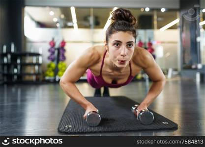 Woman doing push-ups with dumbbells in a fitness workout. Woman doing push-ups exercise with dumbbell in a fitness workout