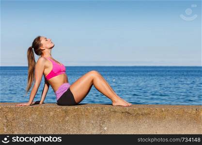 Woman doing sports outdoors. Fitness girl in sportswear on seaside exercising keep her body muscles fit. Woman doing sports exercises outdoors by seaside