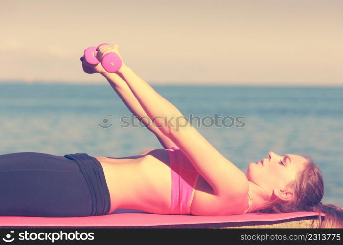 Woman doing sports outdoors with dumbbells. Fit fitness girl in sportswear on seaside exercising. Woman doing sports outdoors with dumbbells