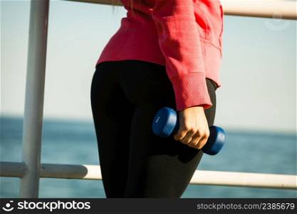 Woman doing sports outdoors with dumbbells. Fit fitness girl in sportswear on seaside exercising . Woman doing sports outdoors with dumbbells