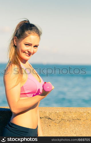 Woman doing sports outdoors with dumbbells. Fit fitness girl in sportswear on seaside exercising. Woman doing sports outdoors with dumbbells