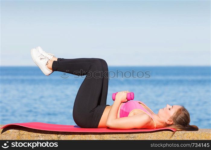 Woman doing sports outdoors with dumbbells. Fit fitness girl in sportswear on seaside exercising. Woman doing sports outdoors with dumbbells