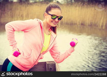 Woman doing sports outdoors with dumbbells lifting weights. Fit fitness girl in sportswear exercising outside on fresh air. Woman exercising with dumbbells outdoor
