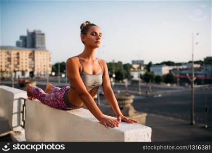 Woman doing yoga exercise, city on background. Yogi meditation workout outdoors. Woman doing yoga exercise, city on background