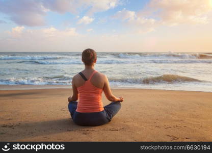 Woman doing yoga - meditating and relaxing in Padmasana Lotus Pose outdoors at tropical beach on sunset. Woman doing yoga Lotus pose oudoors at beach