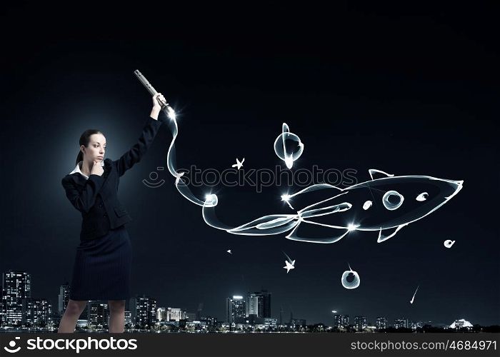 Woman drawing with lantern light. Businesswoman in darkness drawing rocket with flashlight