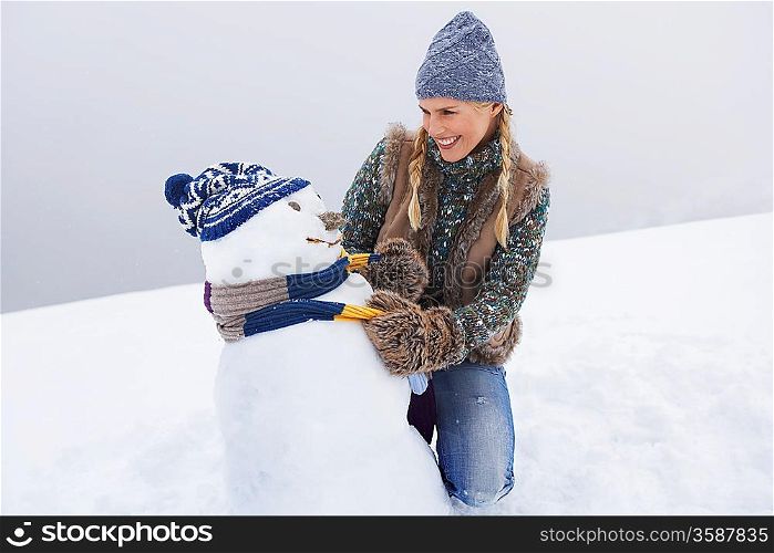 Woman dressing snowman kneeling on snow-covered hill