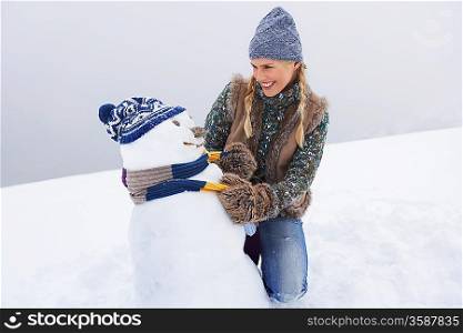 Woman dressing snowman kneeling on snow-covered hill