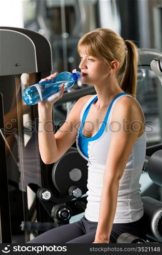 Woman drink water at the gym sitting on fitness machine
