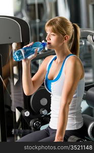 Woman drink water at the gym sitting on fitness machine