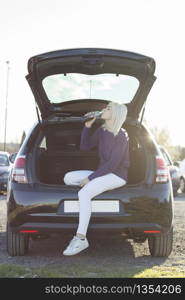 woman drinking a drink sitting on the trunk of a car