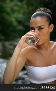 Woman drinking a glass of water by a river