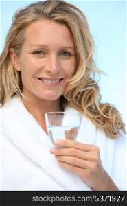 Woman drinking a glass of water in a bathrobe