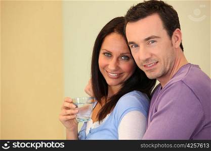 Woman drinking a glass of water in the arms of her husband