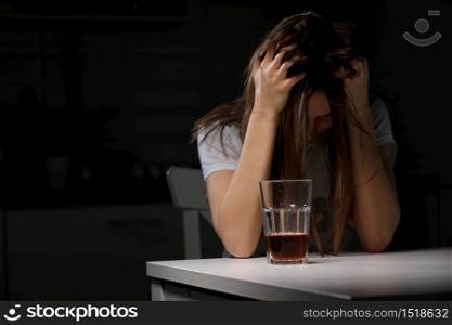 woman drinking alcohol in the kitchen. Young woman suffering from strong headache or migraine sitting with glass of whiskey in the kitchen. alcohol dependence.. woman drinking alcohol in the kitchen. Young woman suffering from strong headache or migraine sitting with glass of whiskey in the kitchen. alcohol dependence