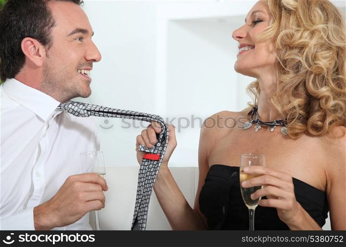 Woman drinking champagne whilst grabbing mans tie