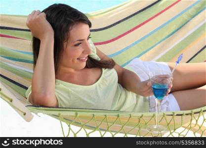 Woman drinking cocktail whilst lying on hammock