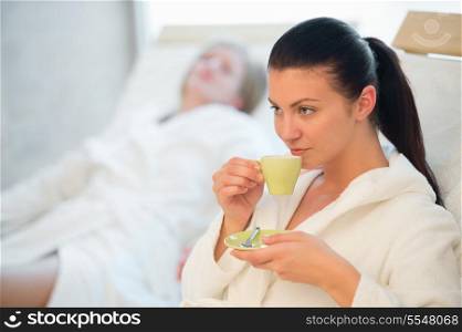Woman drinking coffee at spa with friend in background