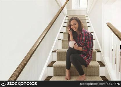 Woman drinking coffee sitting on steps at home and talking on phone