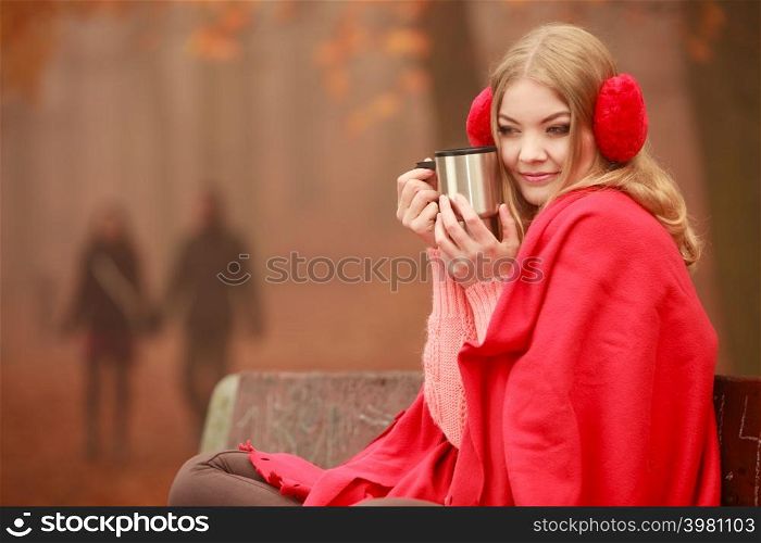 Woman drinking hot coffee or tea relaxing in fall park. Young blonde girl resting outdoor. Autumn lifestyle fun.