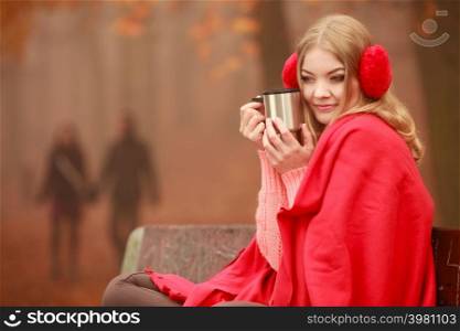 Woman drinking hot coffee or tea relaxing in fall park. Young blonde girl resting outdoor. Autumn lifestyle fun.