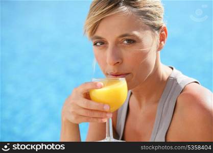 Woman drinking orange juice by swimming pool