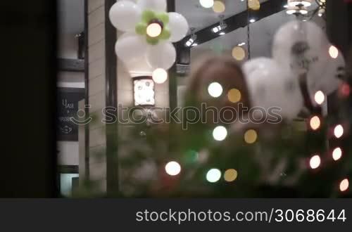 Woman drinking tea and talking on the phone in cafe. View through twinkling Christmas lights. Defocus at the beginning and at the end.