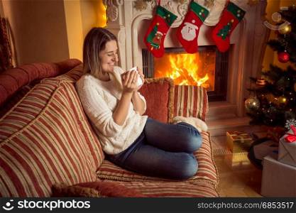 Woman drinking tea at the burning fireplace on Christmas