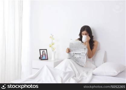 Woman drinking tea while reading a newspaper