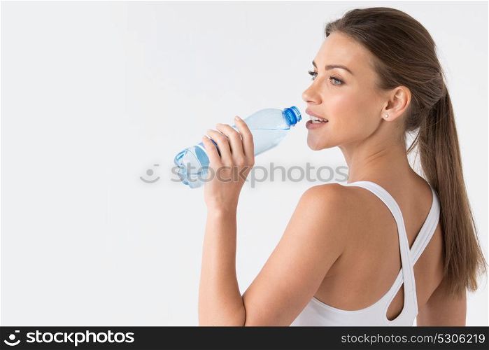 Woman drinking water from blue bottle. Beautiful fit woman drinking water from blue bottle on white background