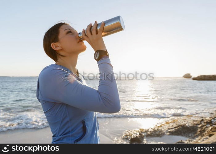 Woman drinking water on beach. Young woman drinking water after exercising on beach