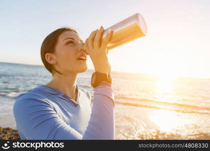 Woman drinking water on beach. Young woman drinking water after exercising on beach