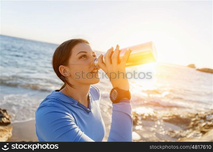 Woman drinking water on beach. Young woman drinking water after exercising on beach