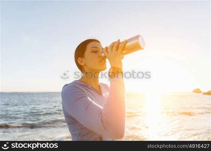 Woman drinking water on beach. Young woman drinking water after exercising on beach