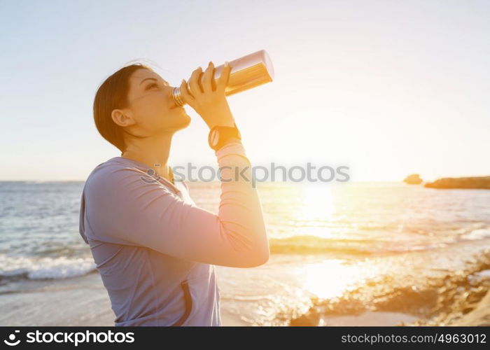 Woman drinking water on beach. Young woman drinking water after exercising on beach