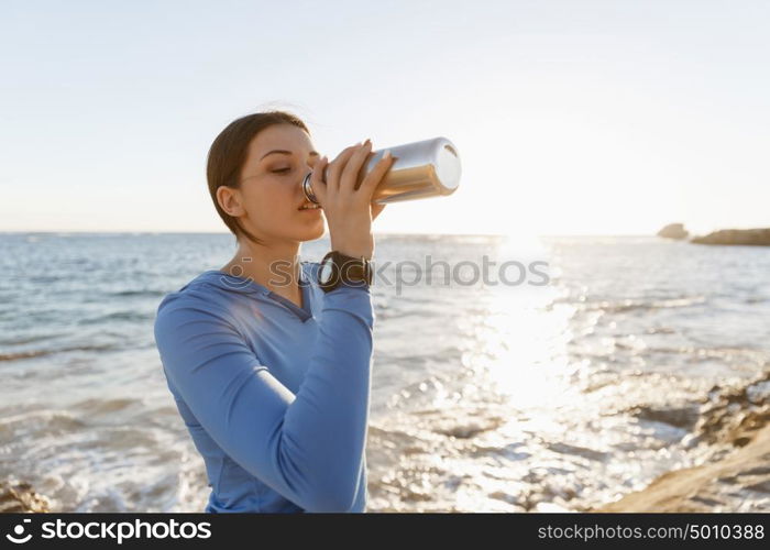 Woman drinking water on beach. Young woman drinking water after exercising on beach