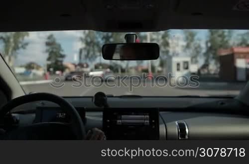 Woman driving car and making a left turn on motorway from secondary road on crossroad against blurry urbanscape background. View inside out of auto.