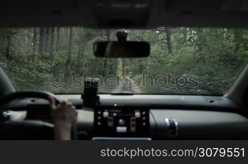 Woman driving car off-road throung the forest in sunligt. View from inside of vehicle. Tourist driver driving auto through green forest on muddy ground path during summer vacation trip