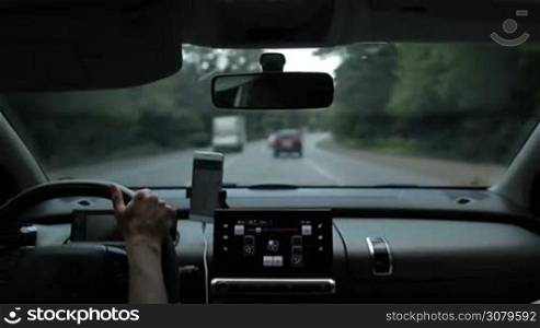 Woman driving car on busy motorway with blurry green forest and traffic on background. View from vehicle&acute;s interior. Experienced female driver controlling auto with one hand while travelling by car on highway.