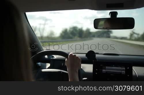 Woman driving car on empty highway on sunny summer day with blurred rural scene on background. View from inside out of vehicle&acute;s interior. Young female travelling by auto on motorway.