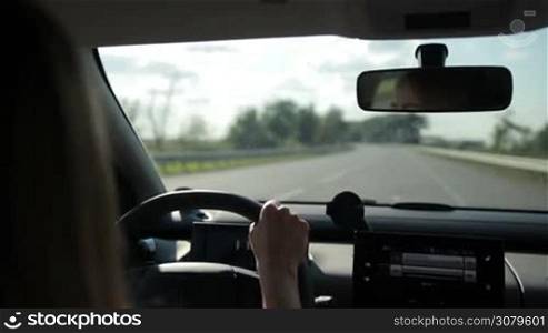 Woman driving car on empty highway on sunny summer day with blurred rural scene on background. View from inside out of vehicle&acute;s interior. Young female travelling by auto on motorway.